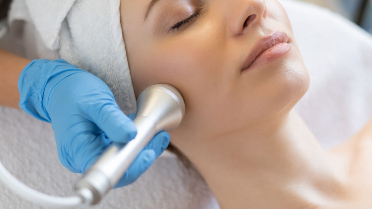 Young woman receiving a non-surgical facelift treatment at a clinic in Riyadh, cosmetologist performing skin rejuvenation on neck and face.
